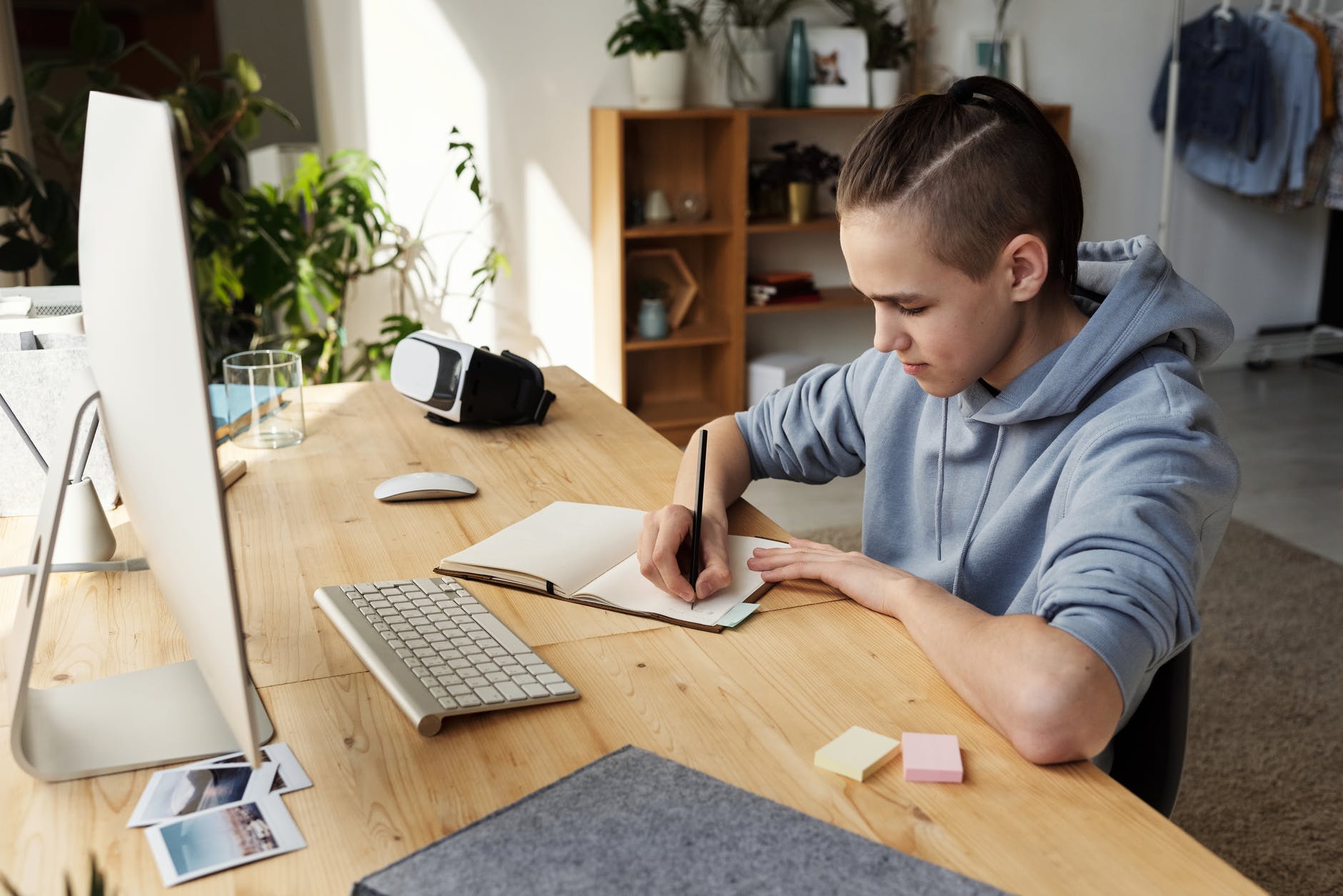 boy in gray hoodie while writing on his notebook